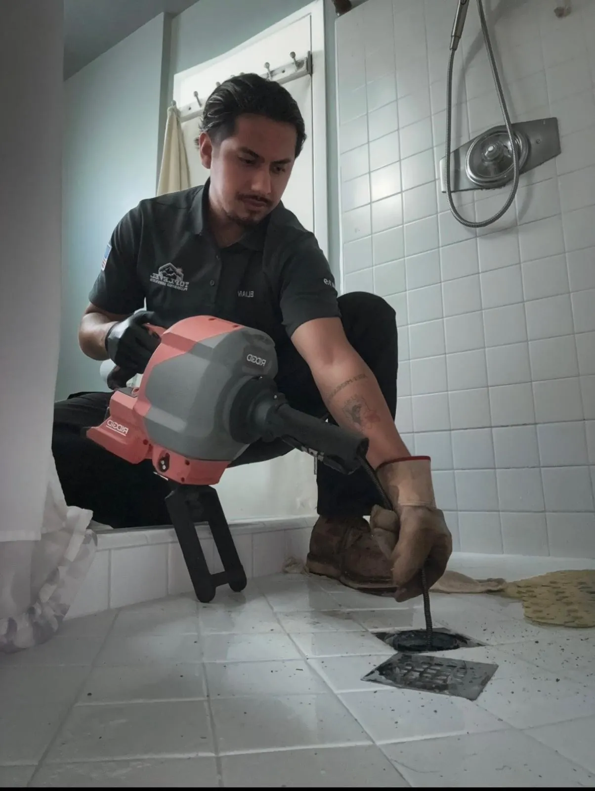 Plumber snaking a shower drain with a drum machine